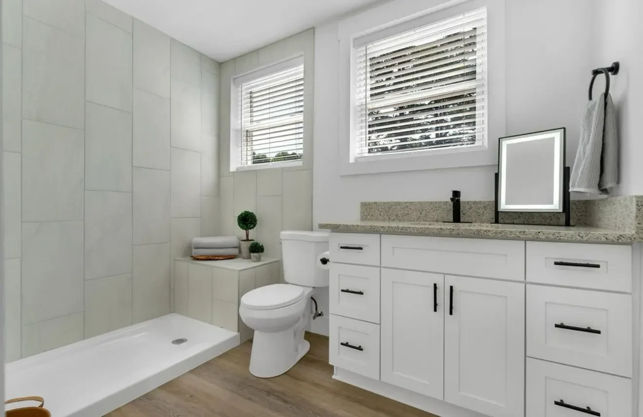Bathroom project with large pale shower tiles, a white vanity and wood-look floor