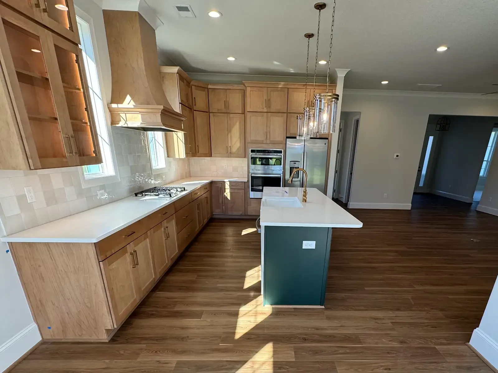 Warm wood flooring beside natural kitchen cabinetry and a green island