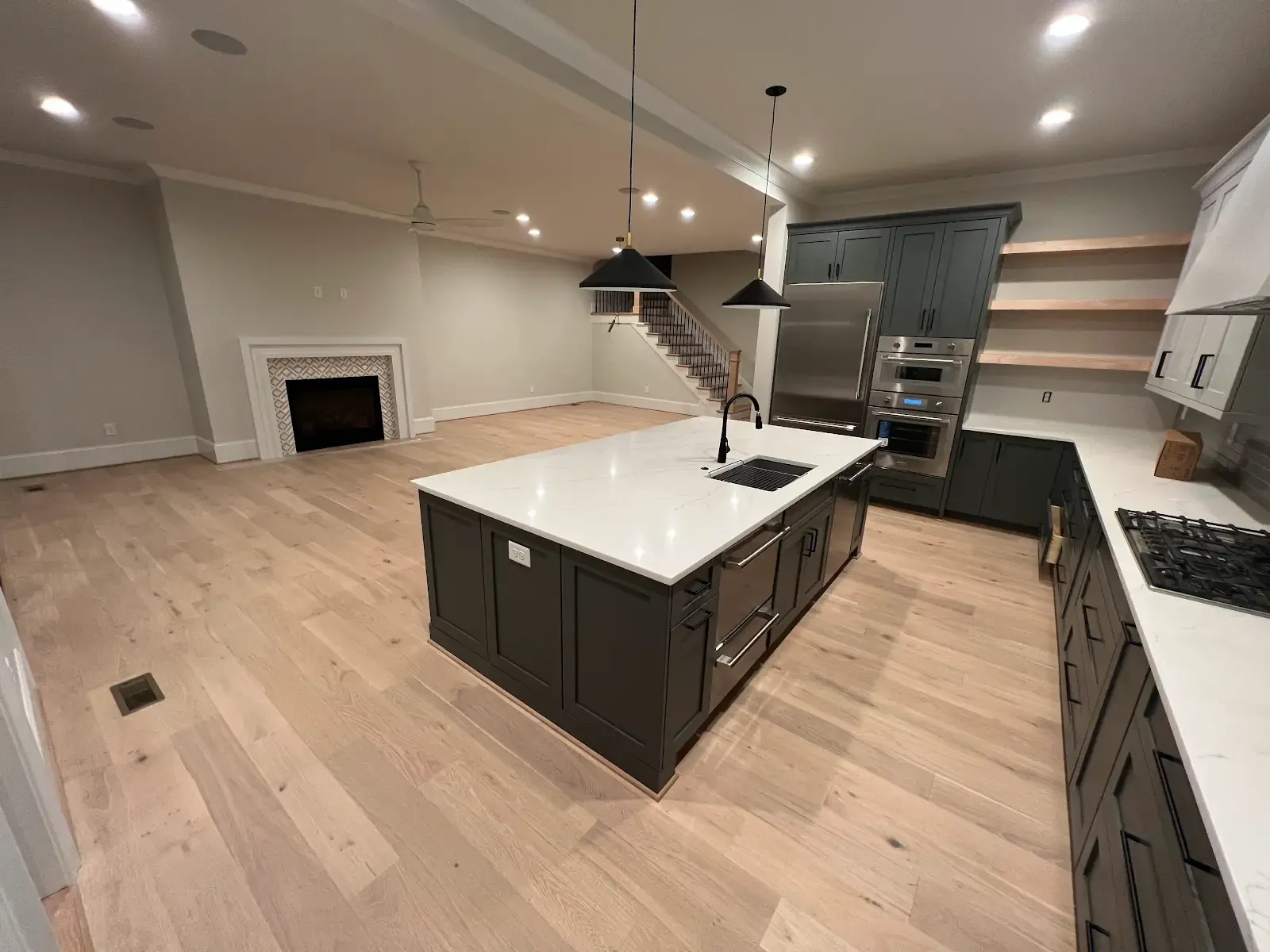 Pale wood flooring connecting a dark-cabinet kitchen and open living room