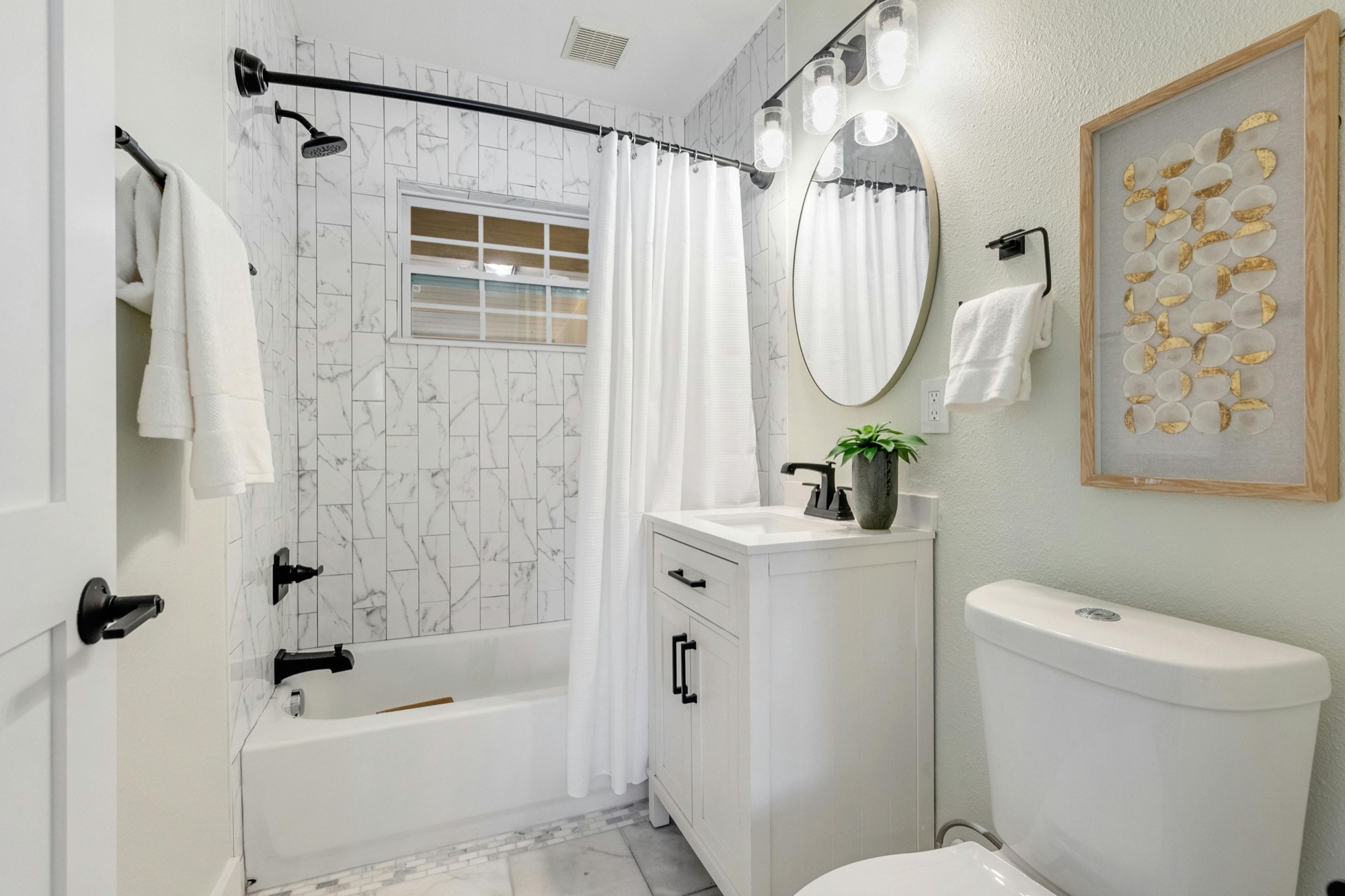 Compact bathroom with tiled tub surround, white vanity and black fittings